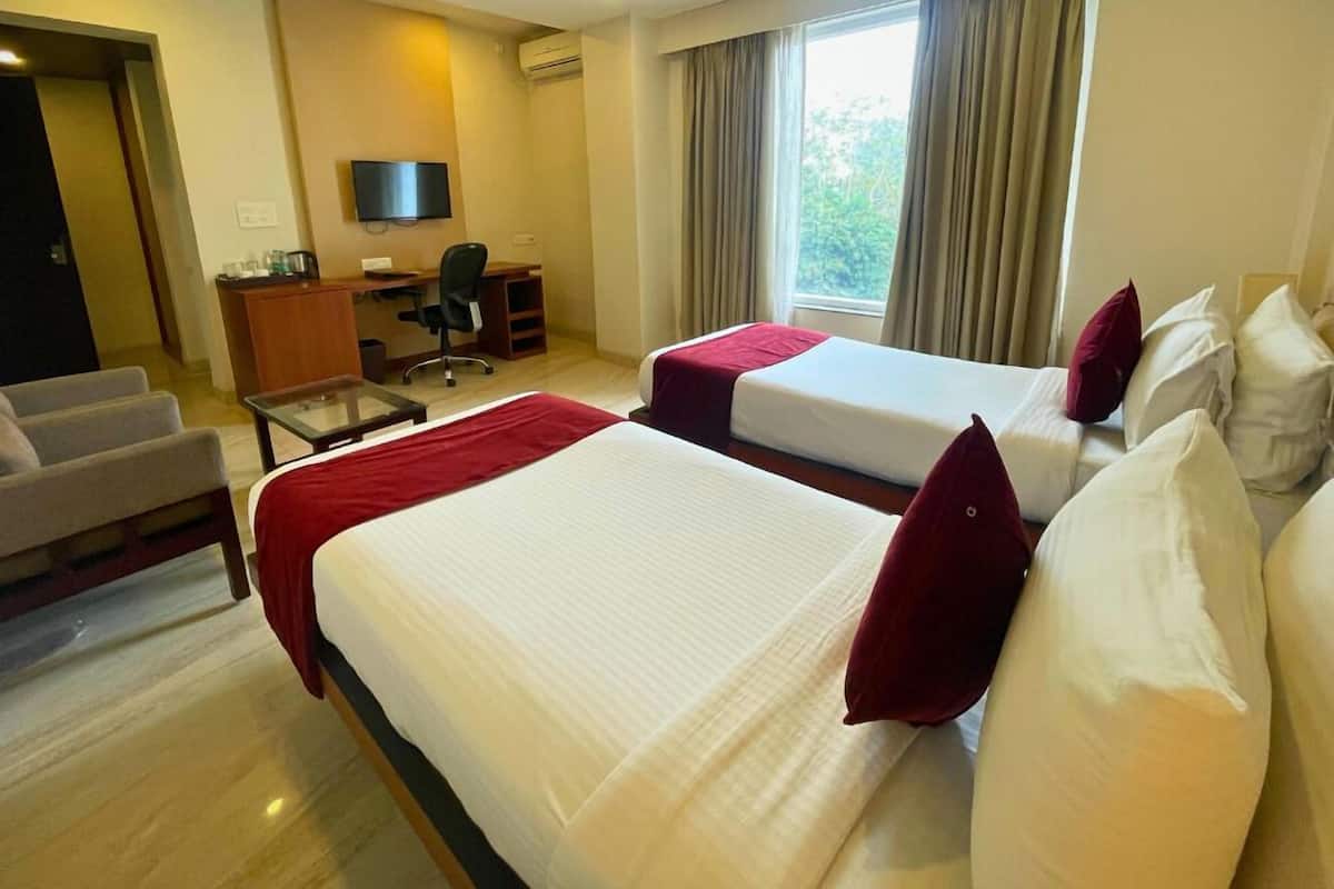 Habitación de hotel con dos camas, un escritorio, una silla, un televisor y una ventana con cortinas.