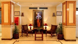 A lobby with two wooden chairs, a small table, and a framed painting on the wall. - Hotel Nandan (Guwahati)