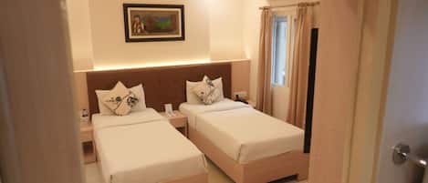 Habitación de hotel con dos camas, una mesita de noche, aire acondicionado instalado en la pared, un cuadro enmarco y una ventana con cortinas.