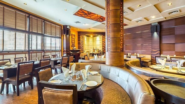 A restaurant with booths, tables, and a central column. - Hotel Nandan (Guwahati)