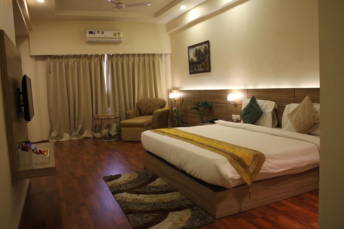 A hotel room with a large bed, a bedside table, a chair, a TV, and a window with curtains.