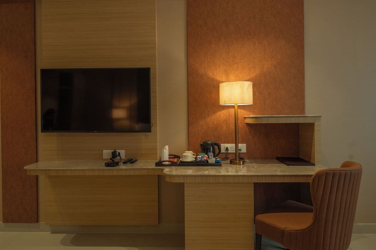 A hotel room with a wooden desk, a flat-screen TV, a lamp, a chair, and a coffee maker.