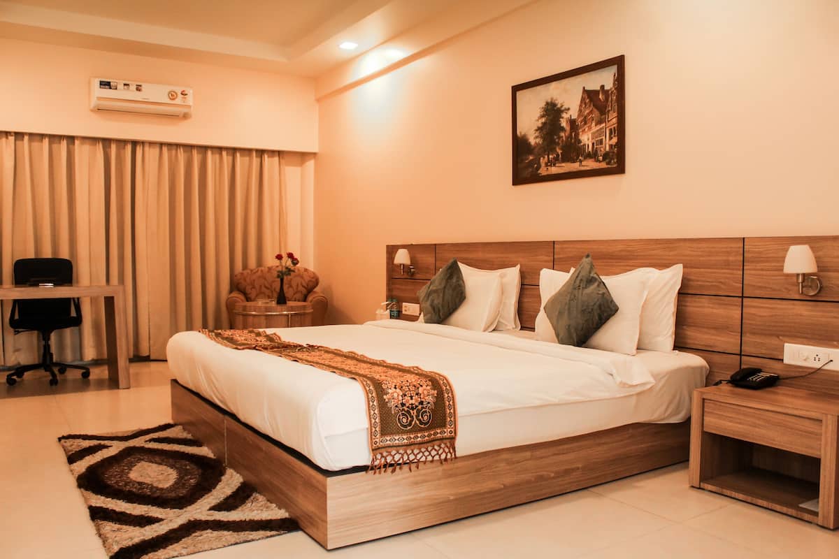 A hotel room with a large bed, a desk, a chair, a nightstand, an air conditioning unit, and a painting on the wall.