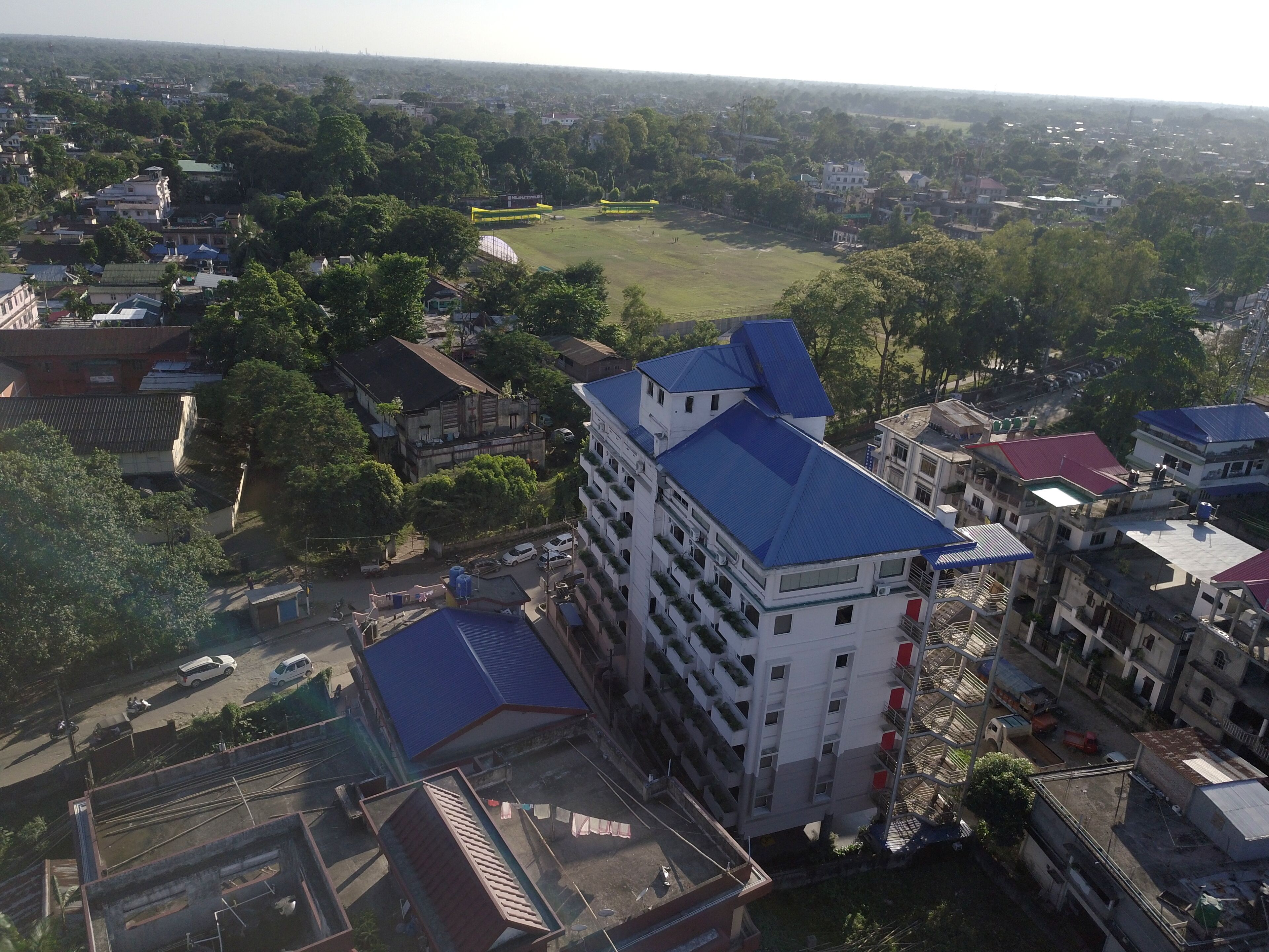 A multi-story building with a blue roof, surrounded by other buildings and greenery.