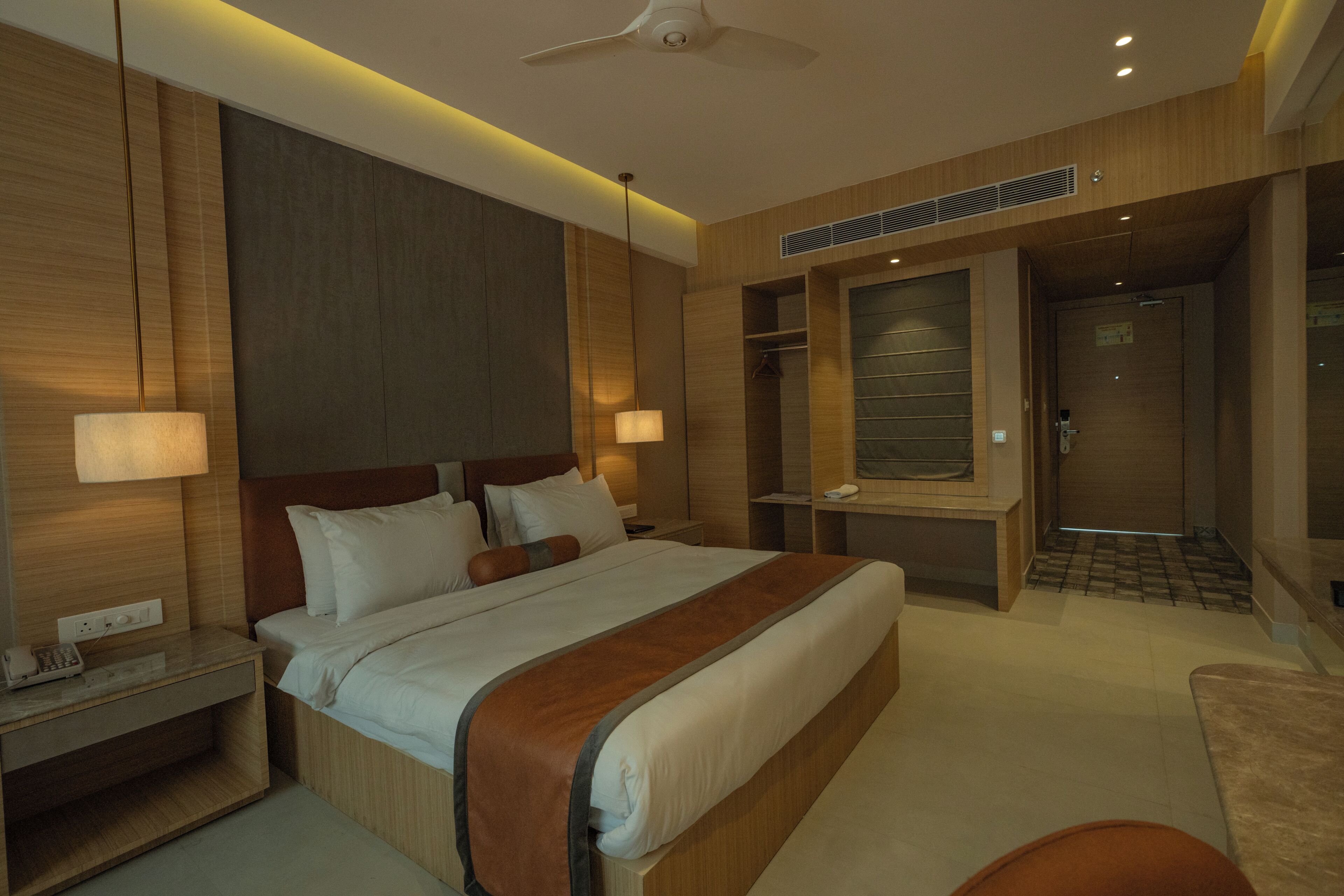 A modern hotel room with a large bed, bedside lamps, a desk, and a wardrobe.