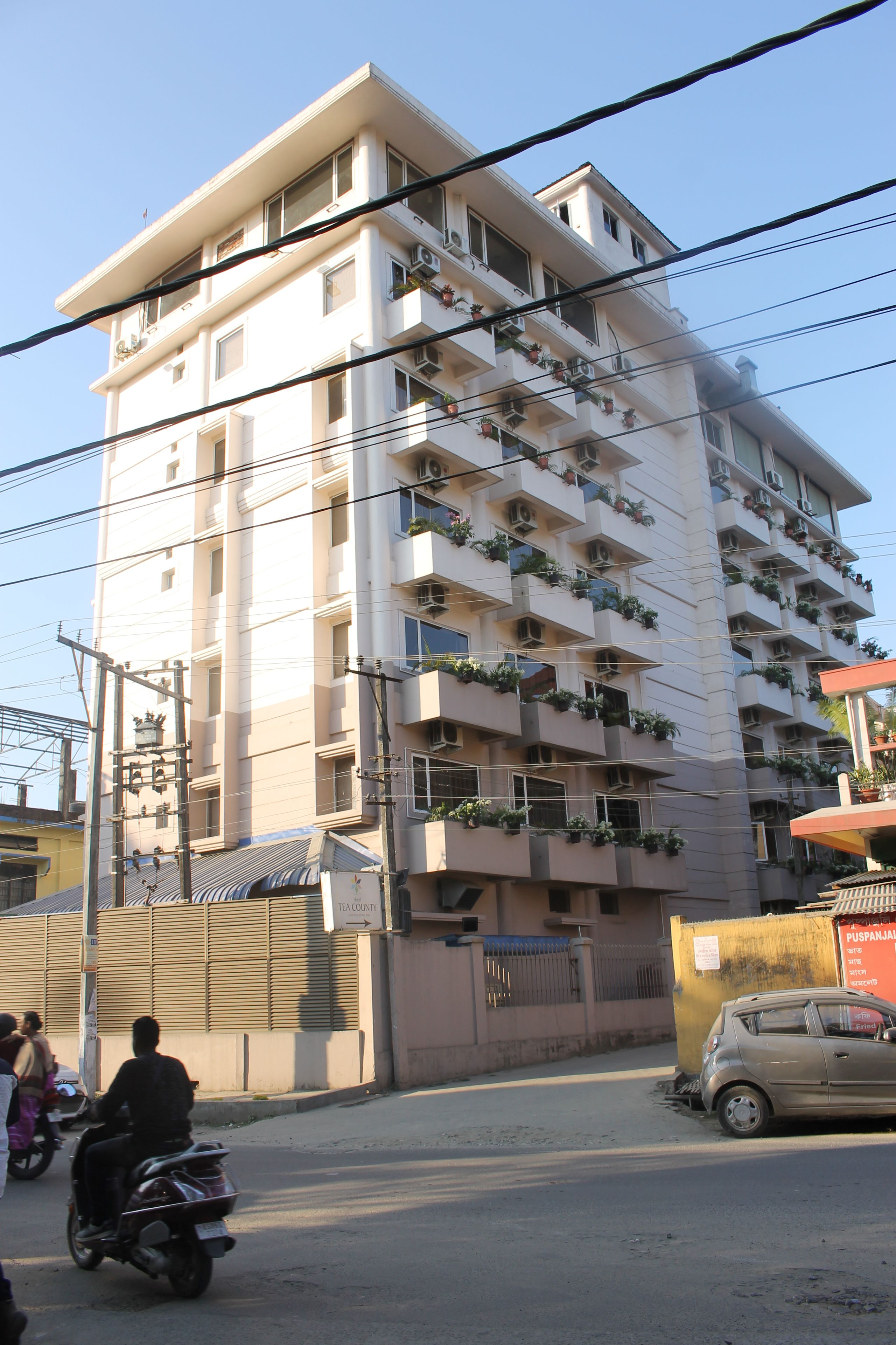 Un edificio de varios pisos con balcones, una entrada con reja y un coche estacionado.