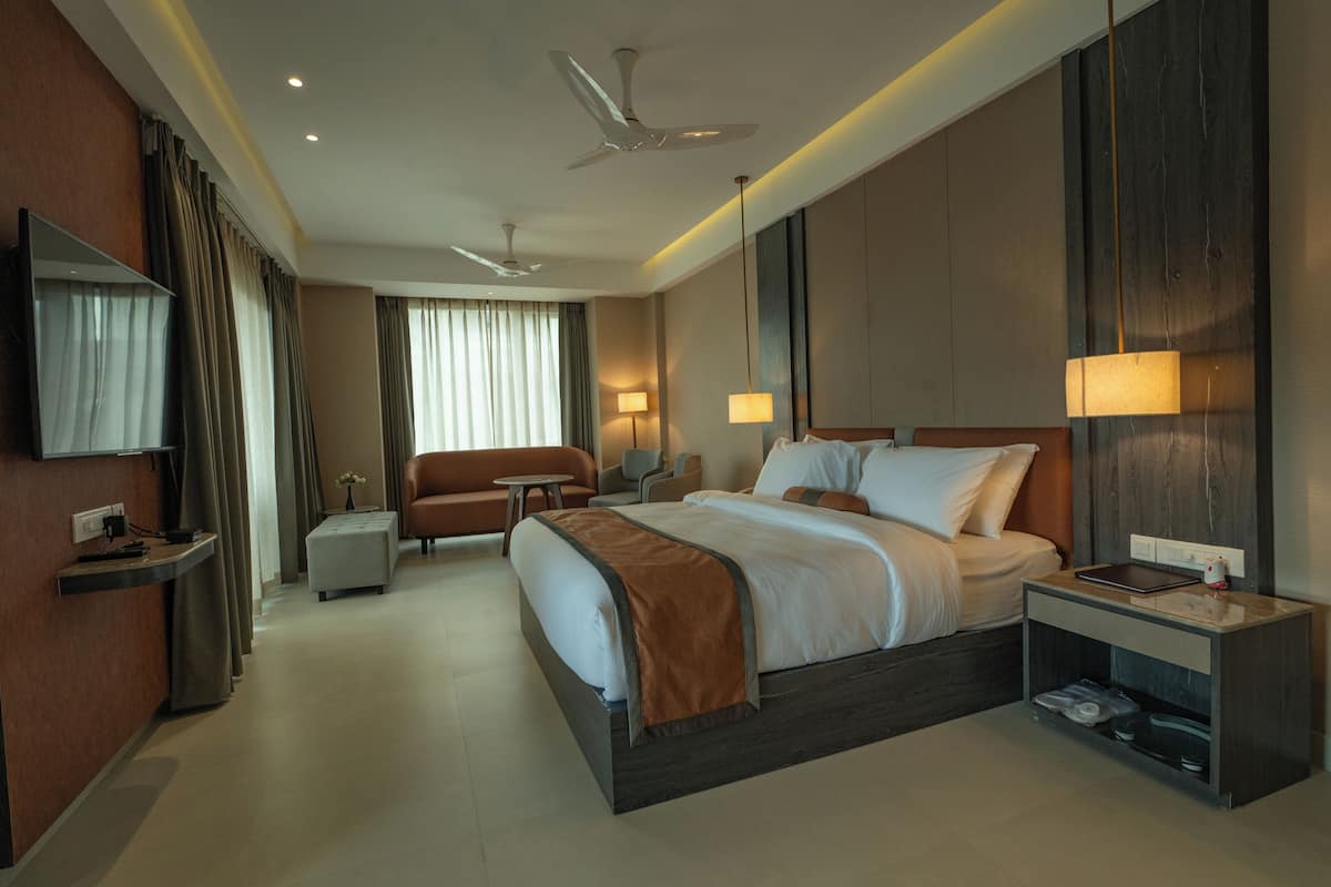 A modern hotel room with a large bed, a desk, a chair, a sofa, and a TV.