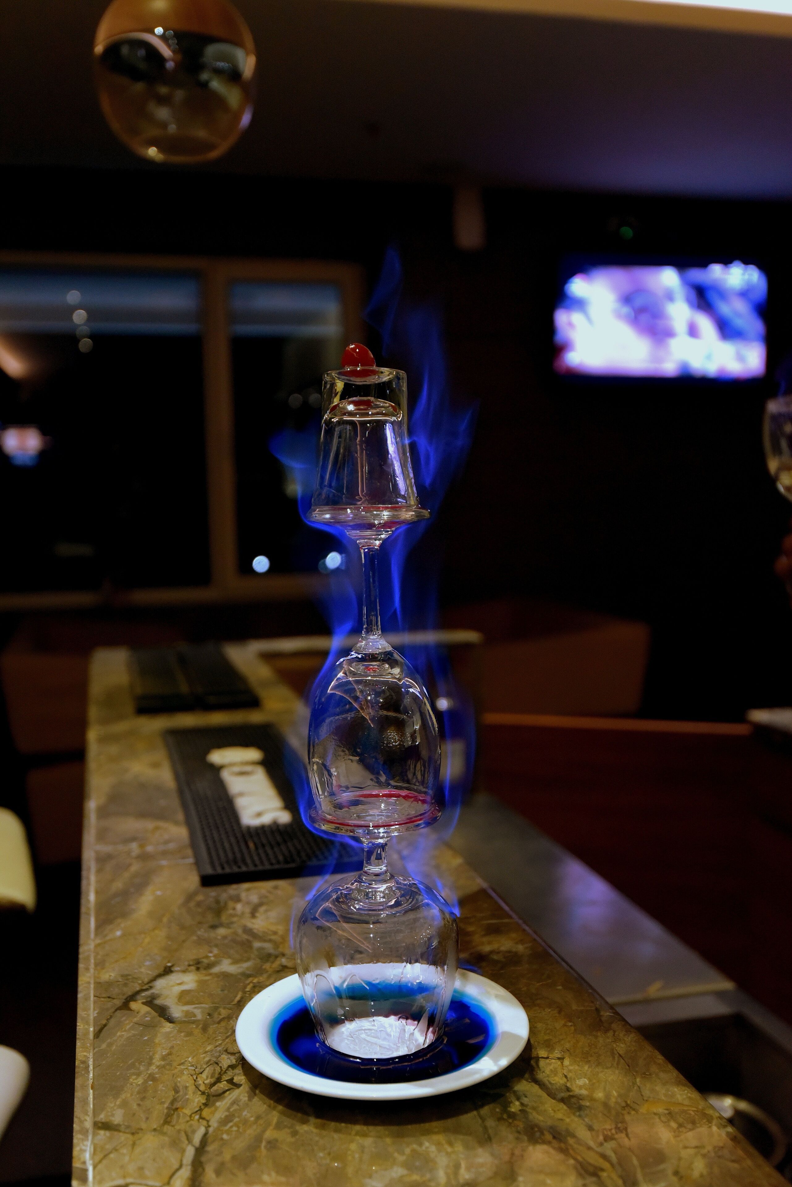 A bar setting with a glass decanter on a coaster, a lit candle, and a television in the background.