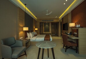 Une chambre d’hôtel équipée d’un lit, d’une table de chevet, d’une lampe, d’une chaise, d’un bureau et d’un ventilateur de plafond.