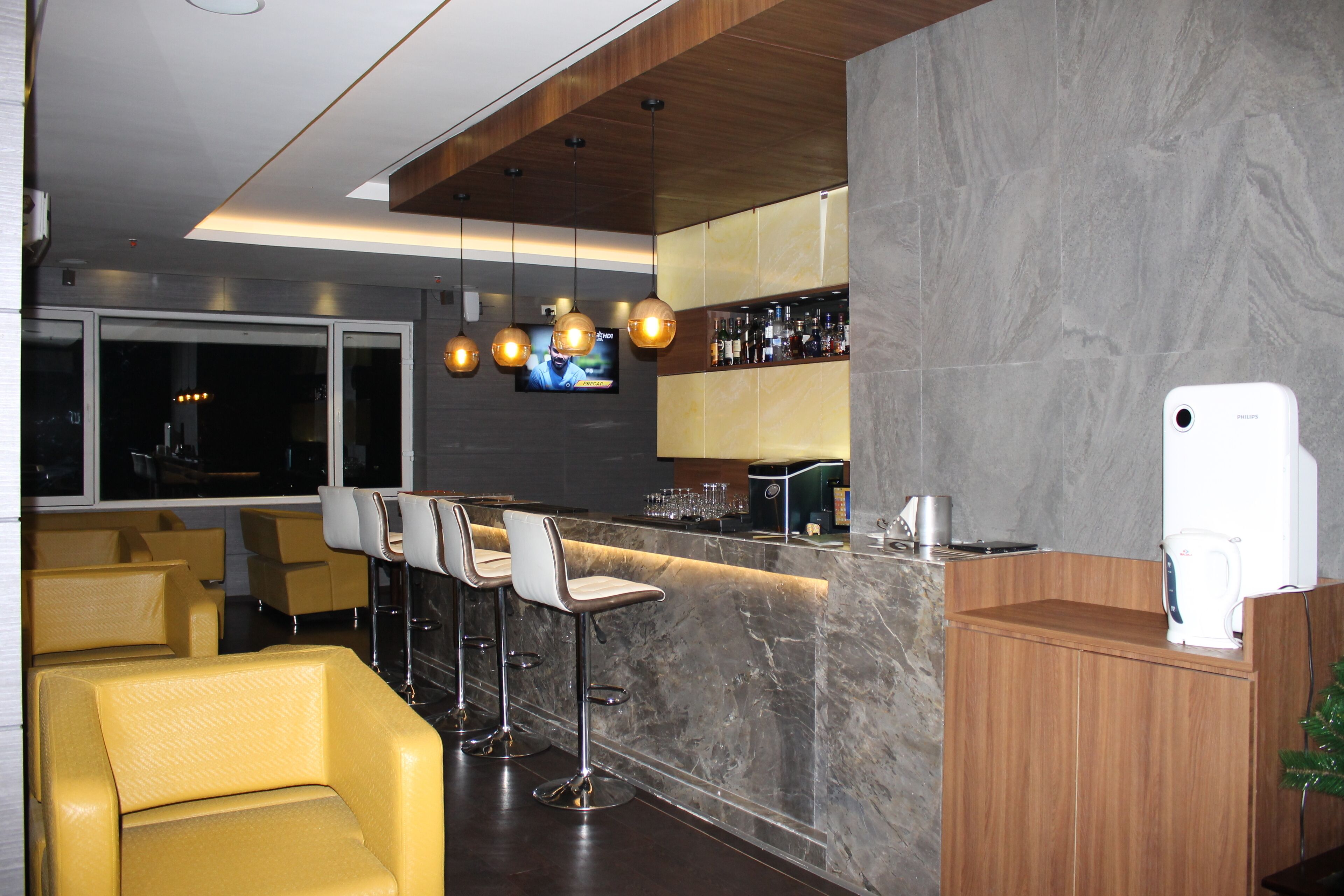 A bar area with a marble countertop, bar stools, and a television mounted on the wall.