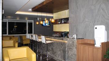A bar area with a marble countertop, bar stools, and a television mounted on the wall.