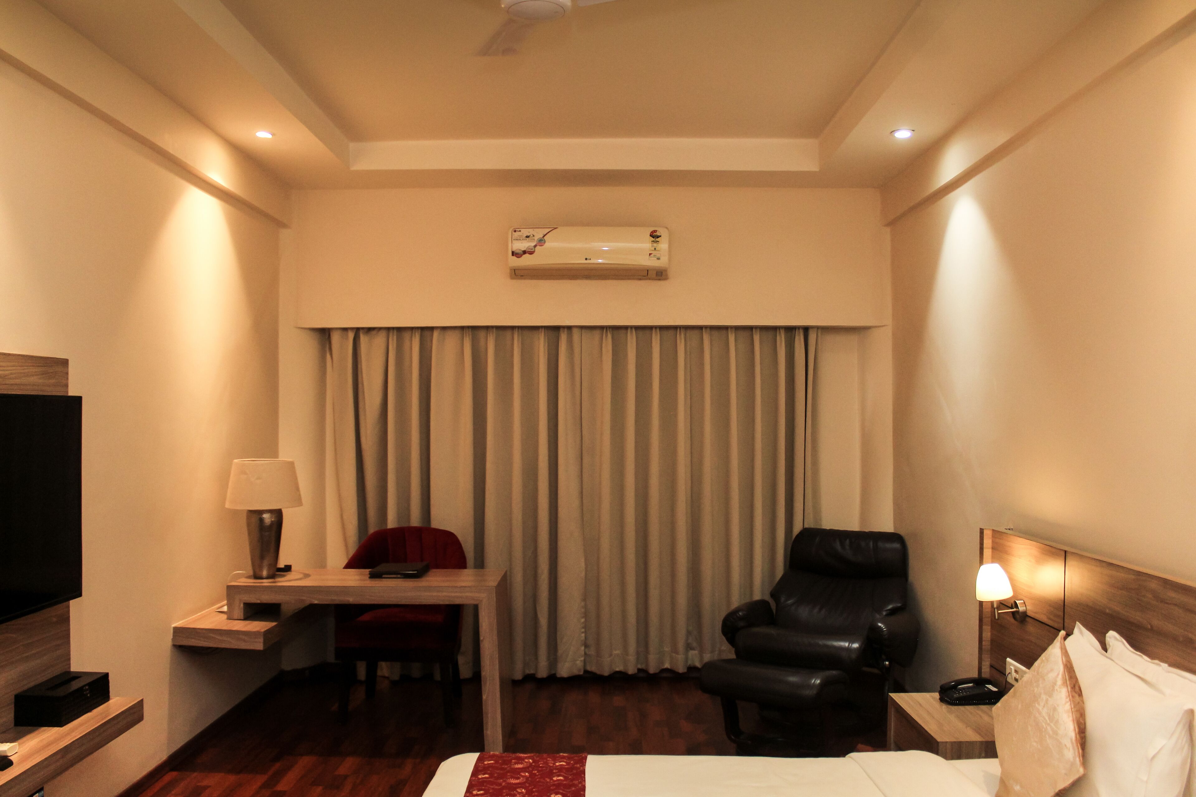Une chambre d’hôtel équipée d’un lit, d’un bureau, d’une chaise, d’une télévision, d’une lampe et d’un ventilateur de plafond.