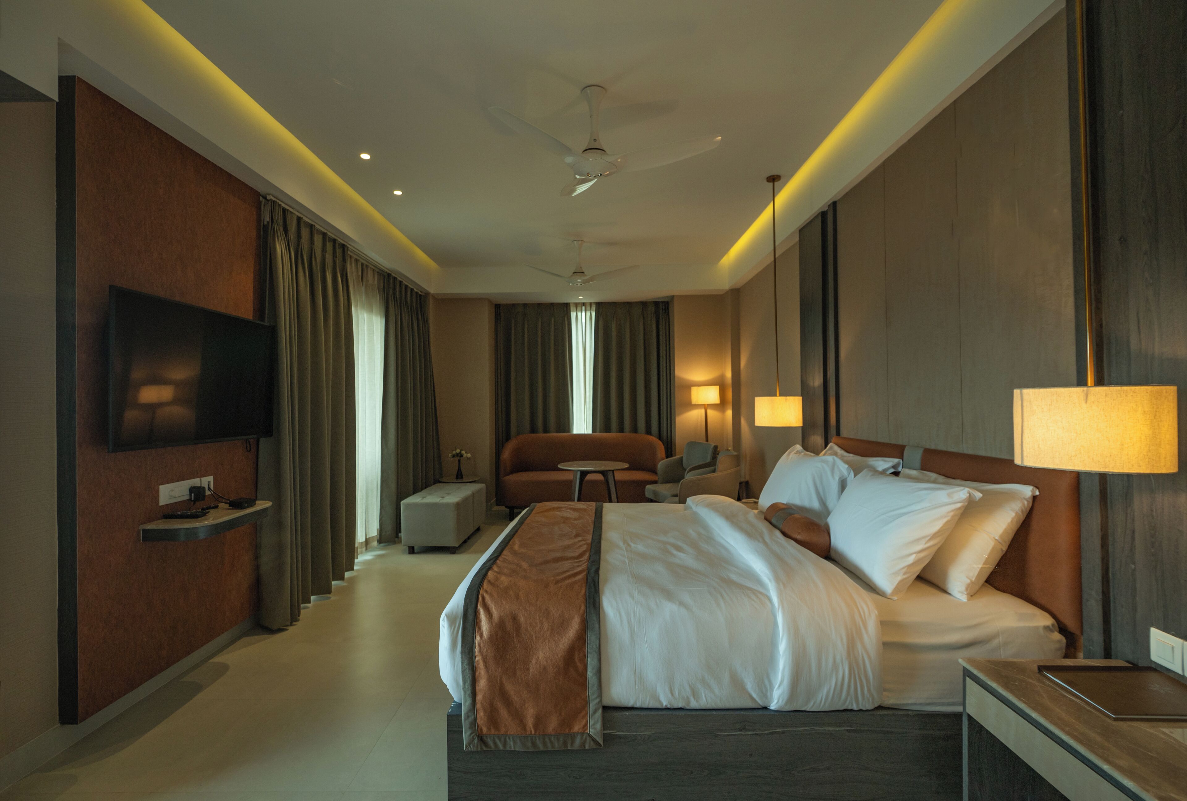 Habitación de hotel con cama, televisor, escritorio, silla, sofá y lámpara.