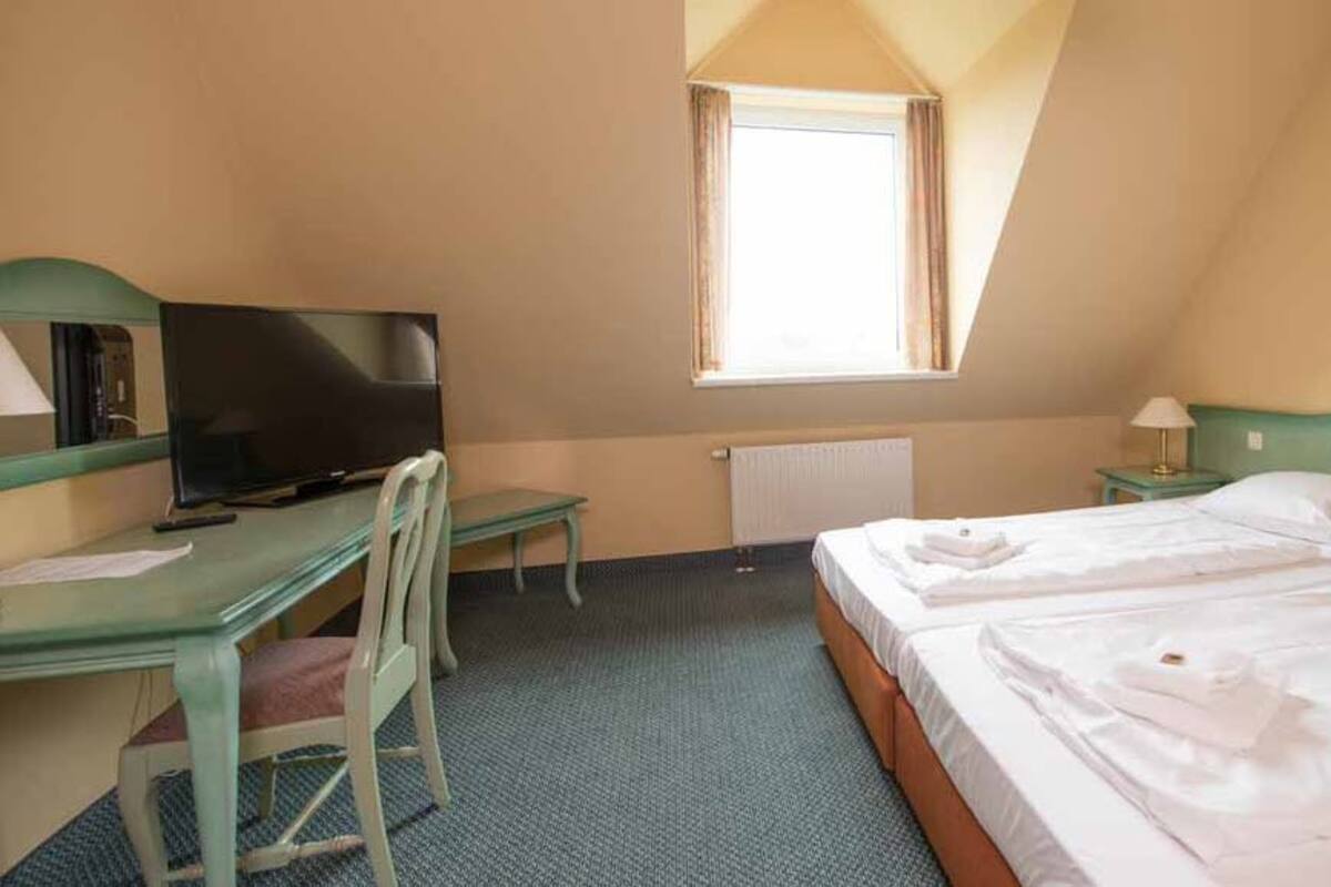Una habitación de hotel con dos camas, un escritorio con silla, televisión y ventana.