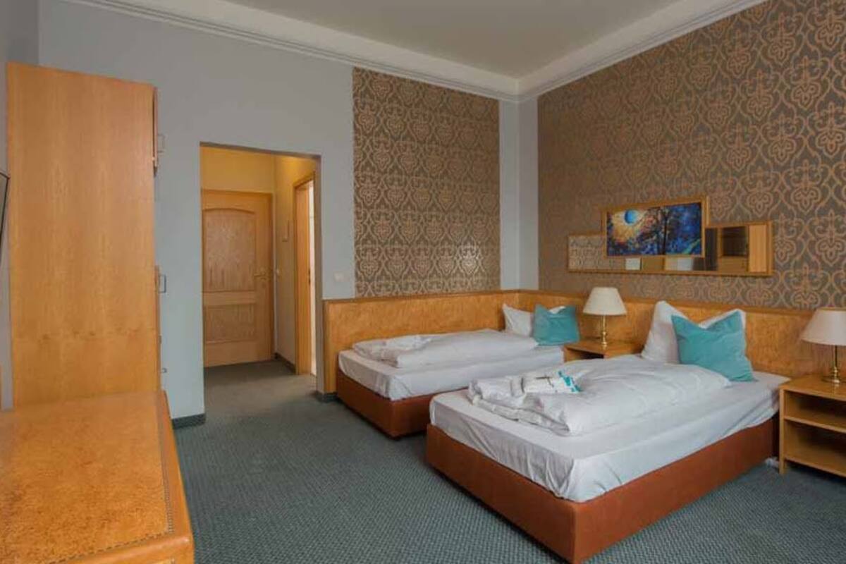 Habitación de hotel con dos camas, un televisor, un escritorio de madera y una puerta que da a otra habitación.