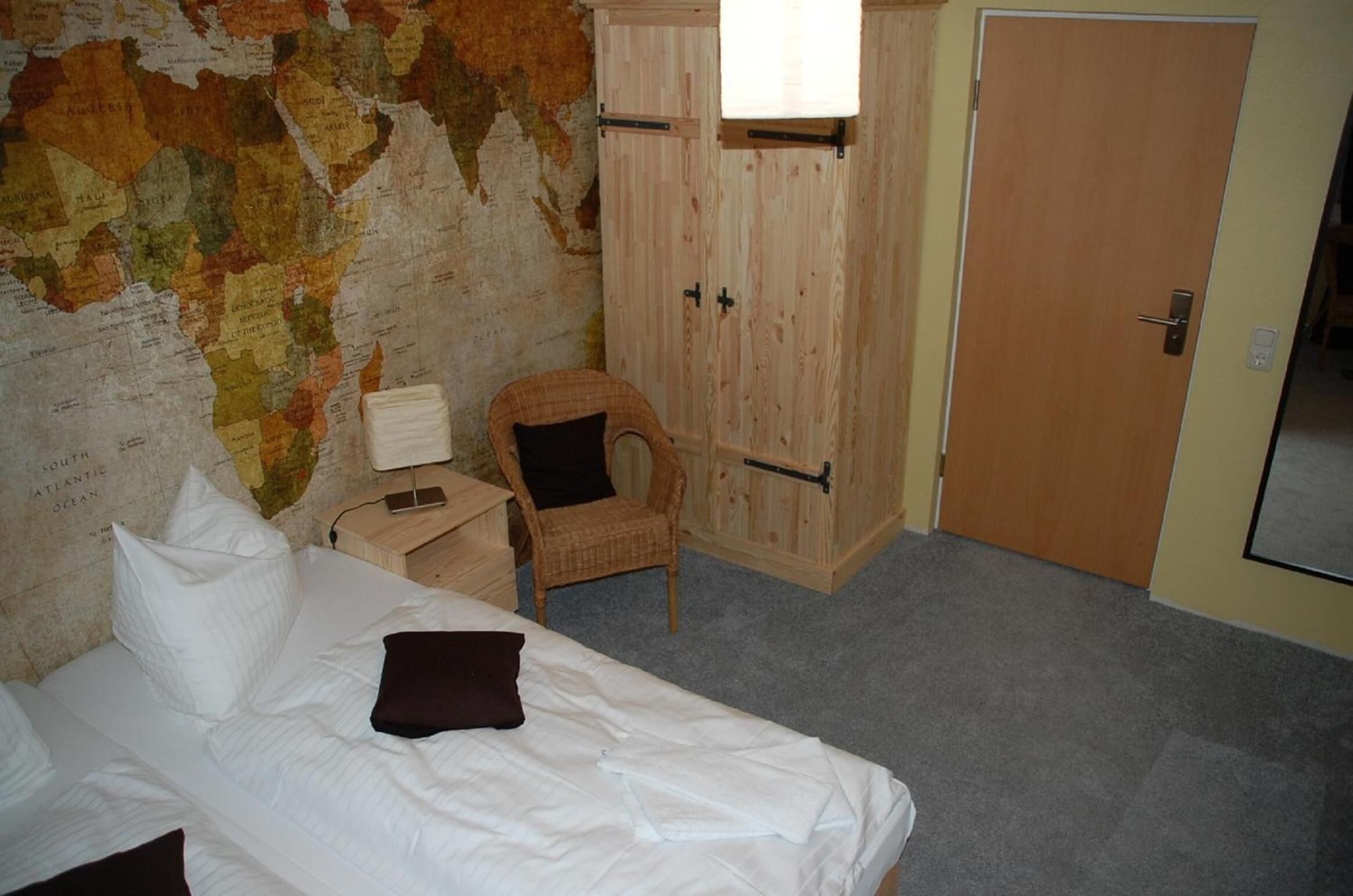 Una habitación con cama, una silla, un armario y un mapa en la pared.