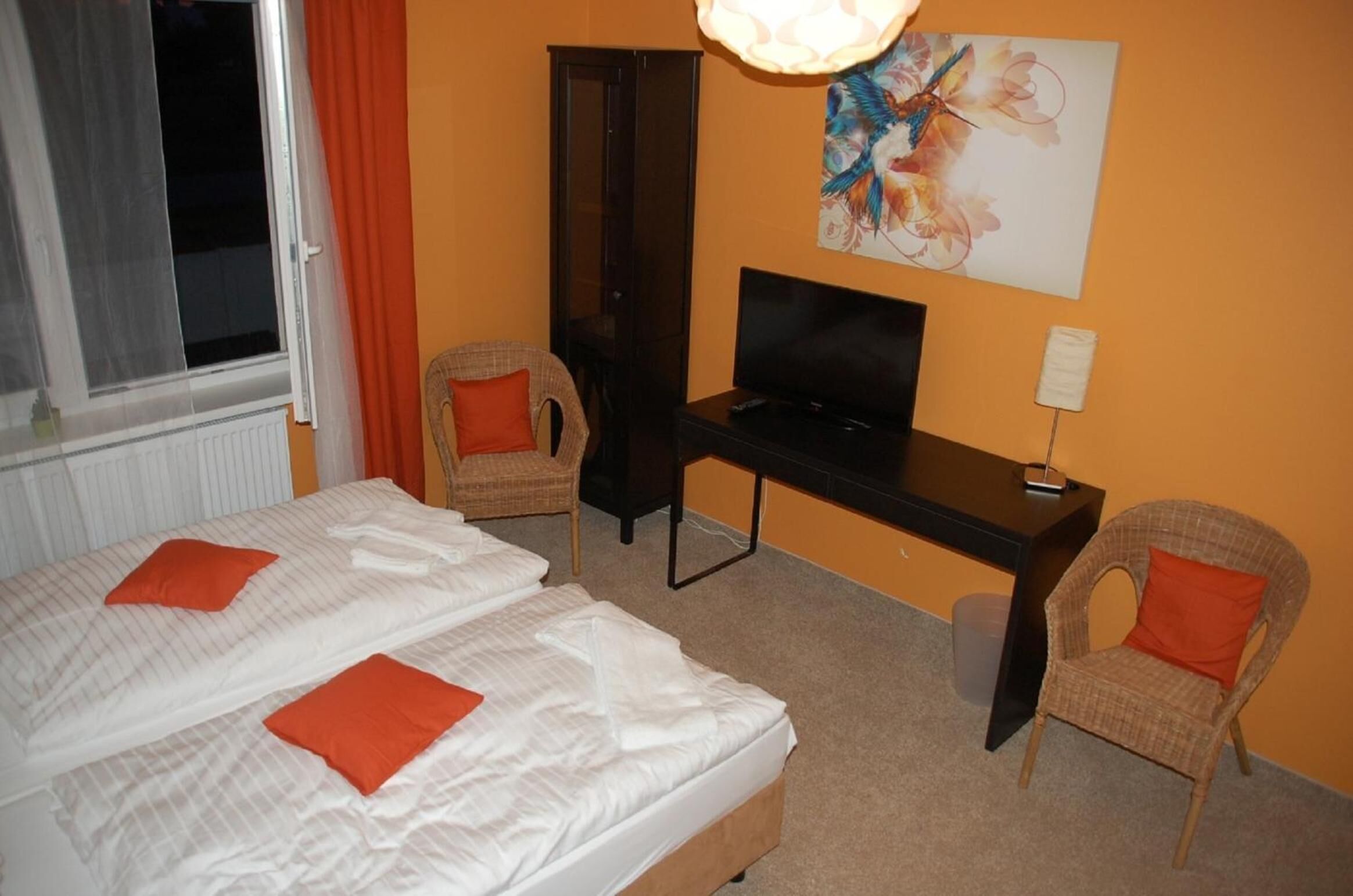 Quarto de hotel com duas camas, uma escrivaninha, televisão e um quadro na parede.