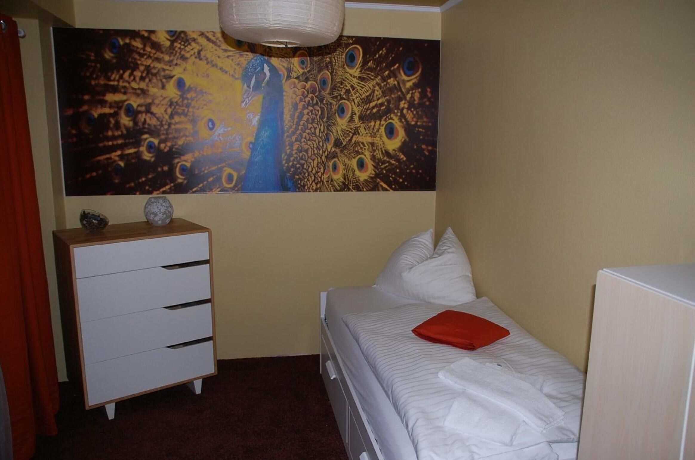 A bedroom with a bed, a dresser, a painting, and a red pillow.
