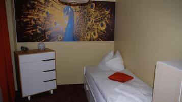 A bedroom with a bed, a dresser, a painting, and a red pillow.