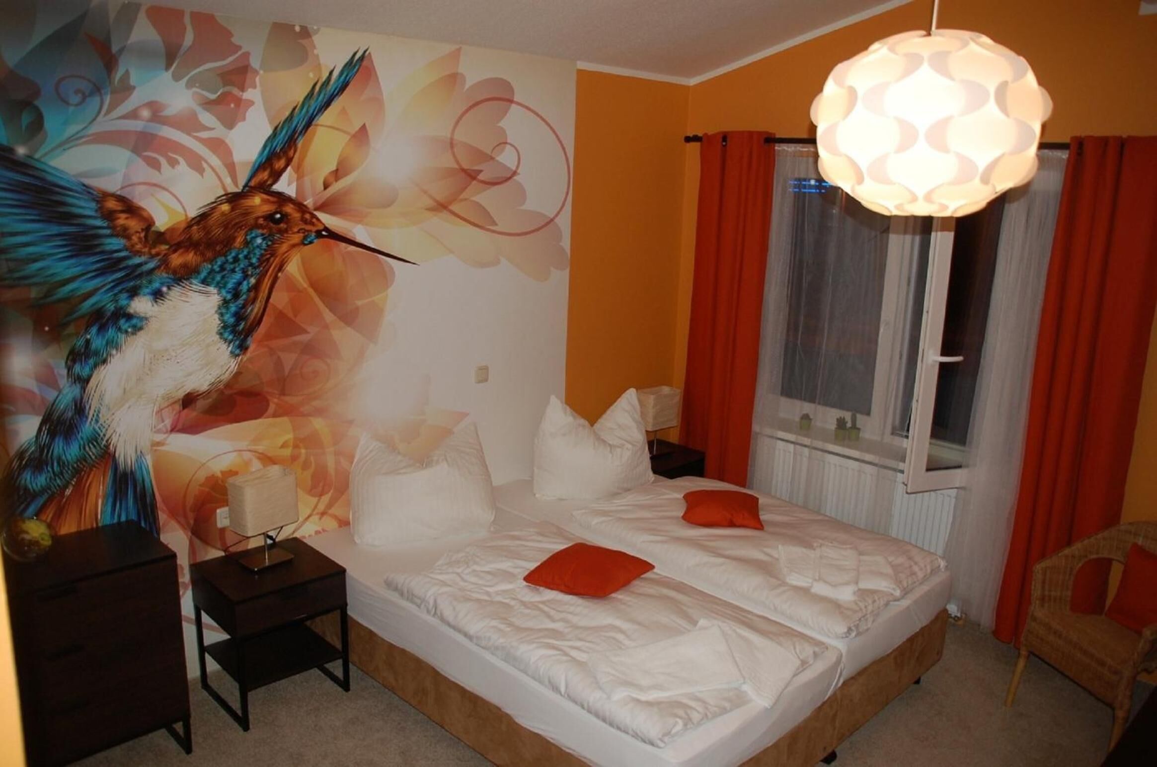 Ein Schlafzimmer mit einem großen Bett, einem Nachttisch, einer Lampe, einem Sessel und einem Fenster mit Vorhängen.