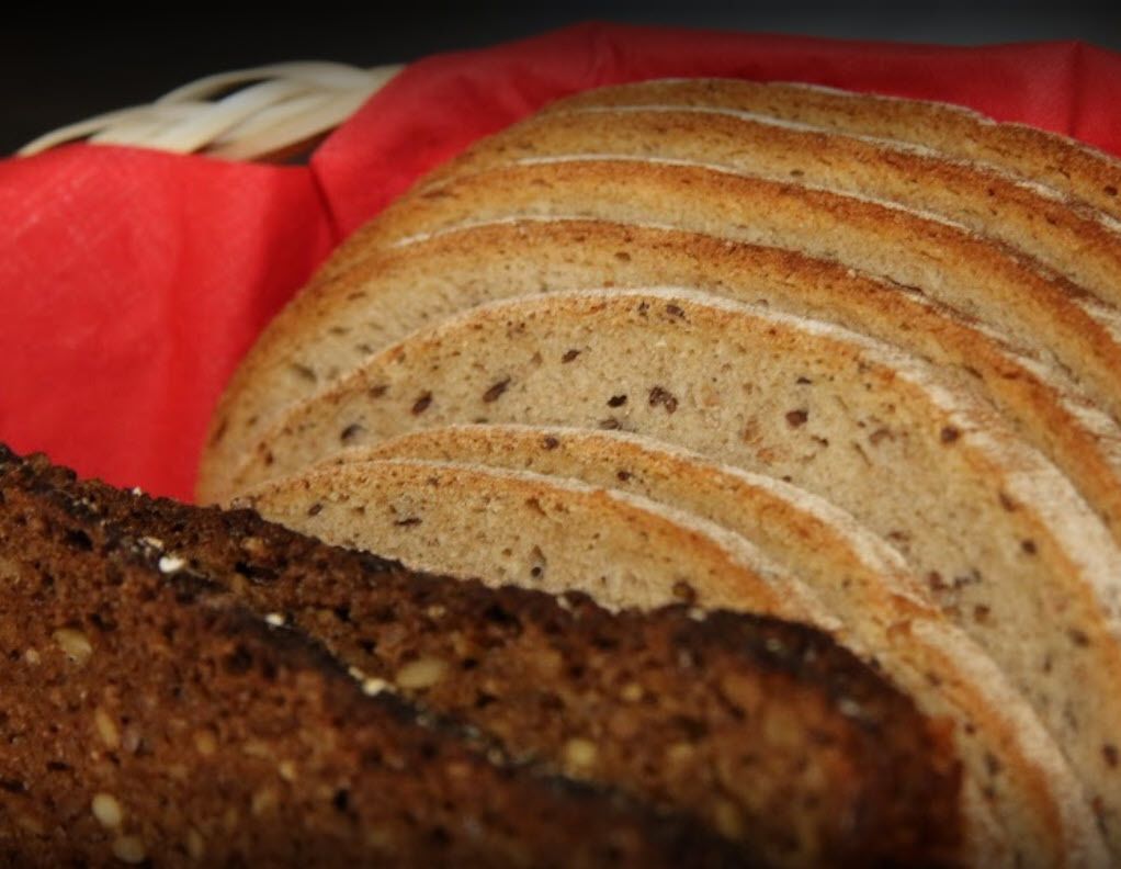 A loaf of sliced bread with a crusty exterior and a dense, dark interior, placed on a red surface.