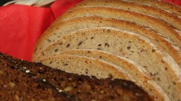 A loaf of sliced bread with a crusty exterior and a dense, dark interior, placed on a red surface.