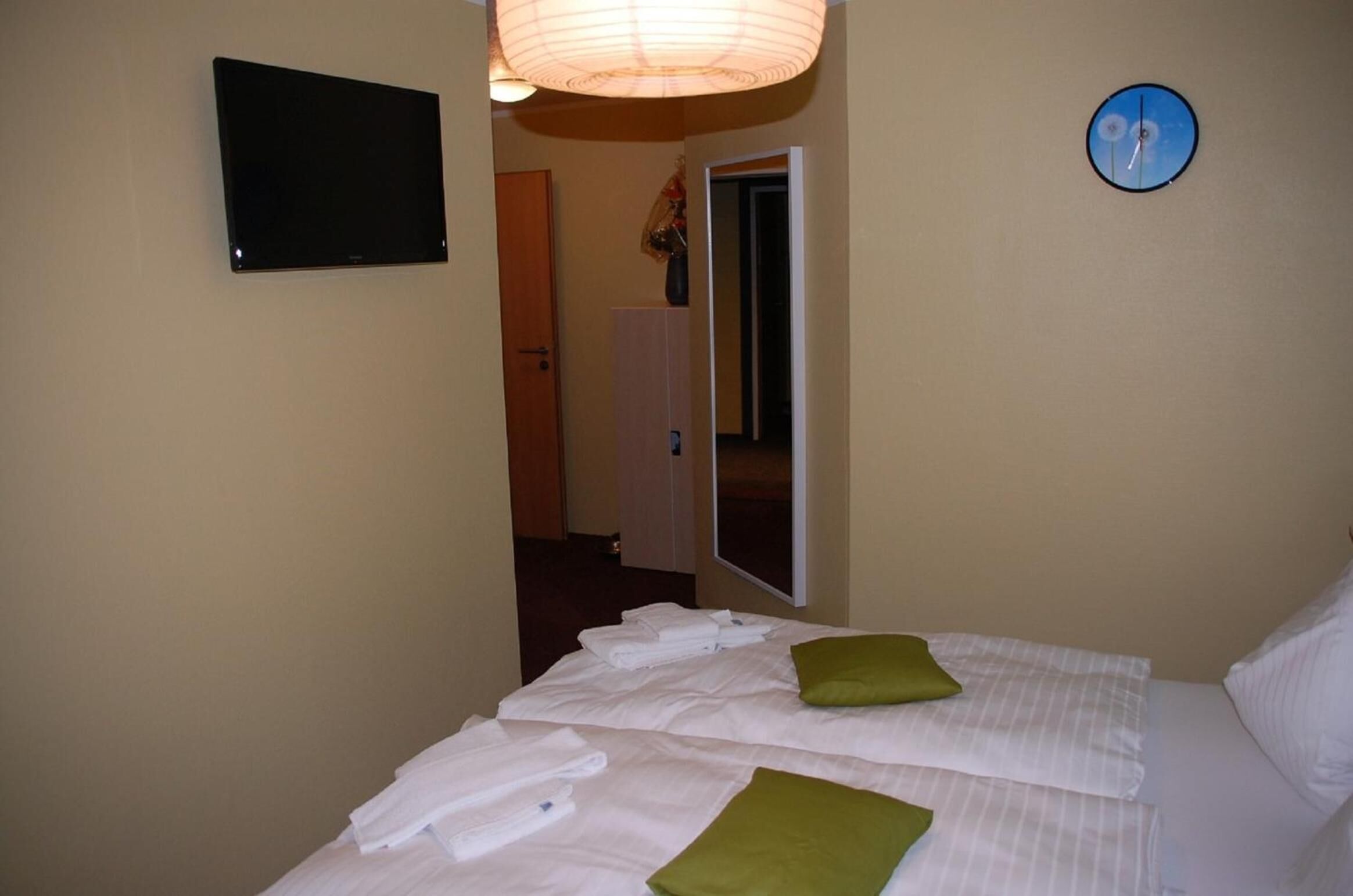 A hotel room with a bed, a flat-screen TV, a clock, and a door leading to another room.