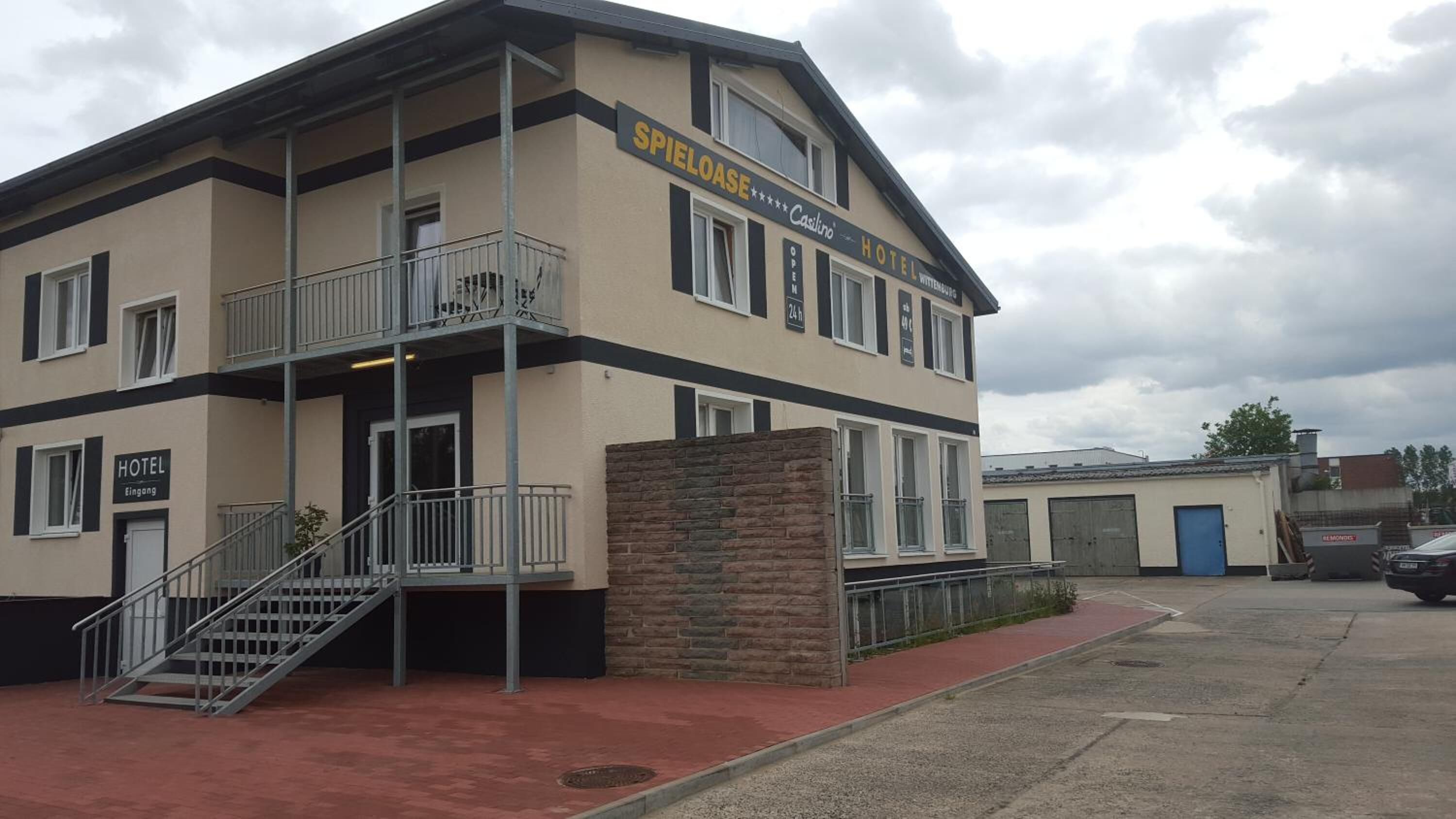 Een gebouw met twee verdiepingen, met een bord voor Spielloase Casillino Hotel, voorzien van een balkon, een stenen gevel en een trap naar de ingang.