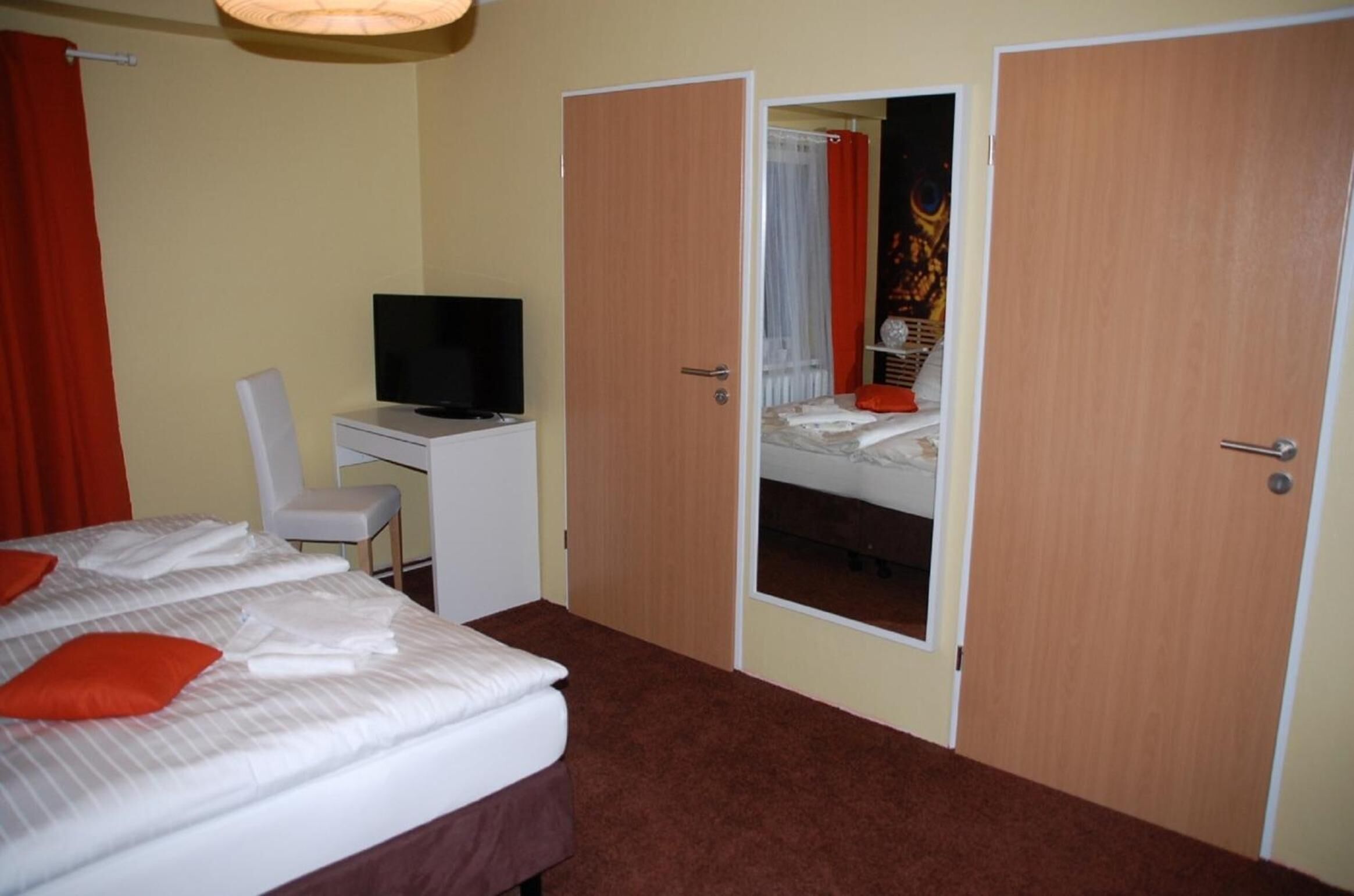 A hotel room with a bed, a desk with a television, and two doors leading to another room.
