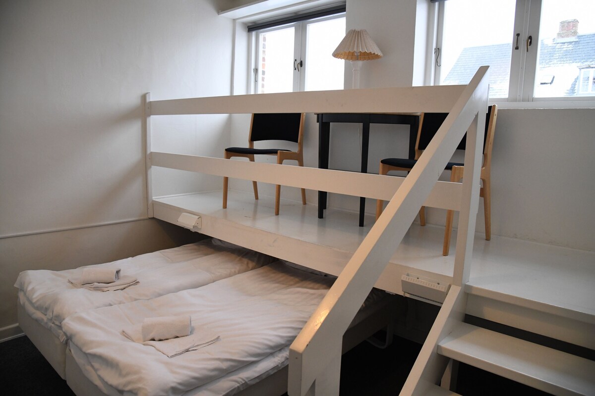 A bunk bed with a desk and chair, a window, and a lamp.