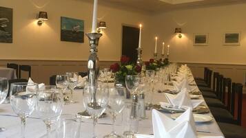 A long dining table set with white tablecloth, candles, and wine glasses, in a room with framed pictures on the walls.