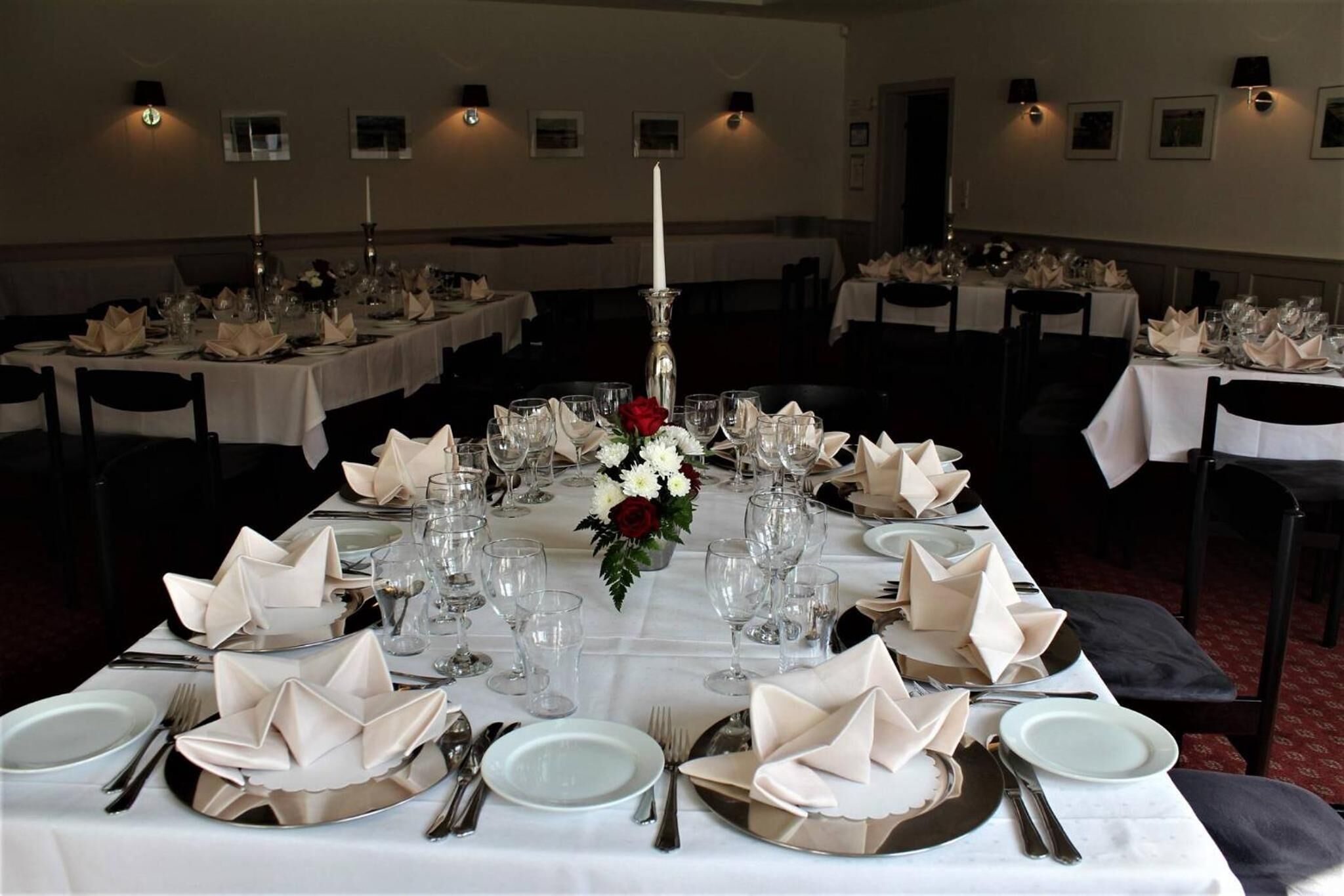 A banquet hall with multiple tables set for a formal event, each with white tablecloths, folded napkins, and candle centerpieces.