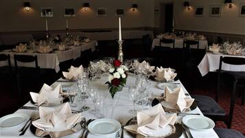 A banquet hall with multiple tables set for a formal event, each with white tablecloths, folded napkins, and candle centerpieces.