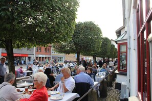 A crowded outdoor dining area with tables and chairs, surrounded by buildings and trees.