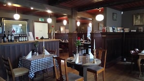 Interior de restaurante con paneles de madera, manteles a cuadros y una zona de bar con botellas y copas de vino.