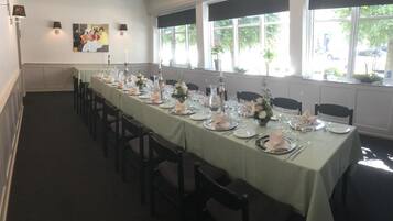 Una larga mesa de comedor con sillas, mantel verde y centros de mesa con flores.