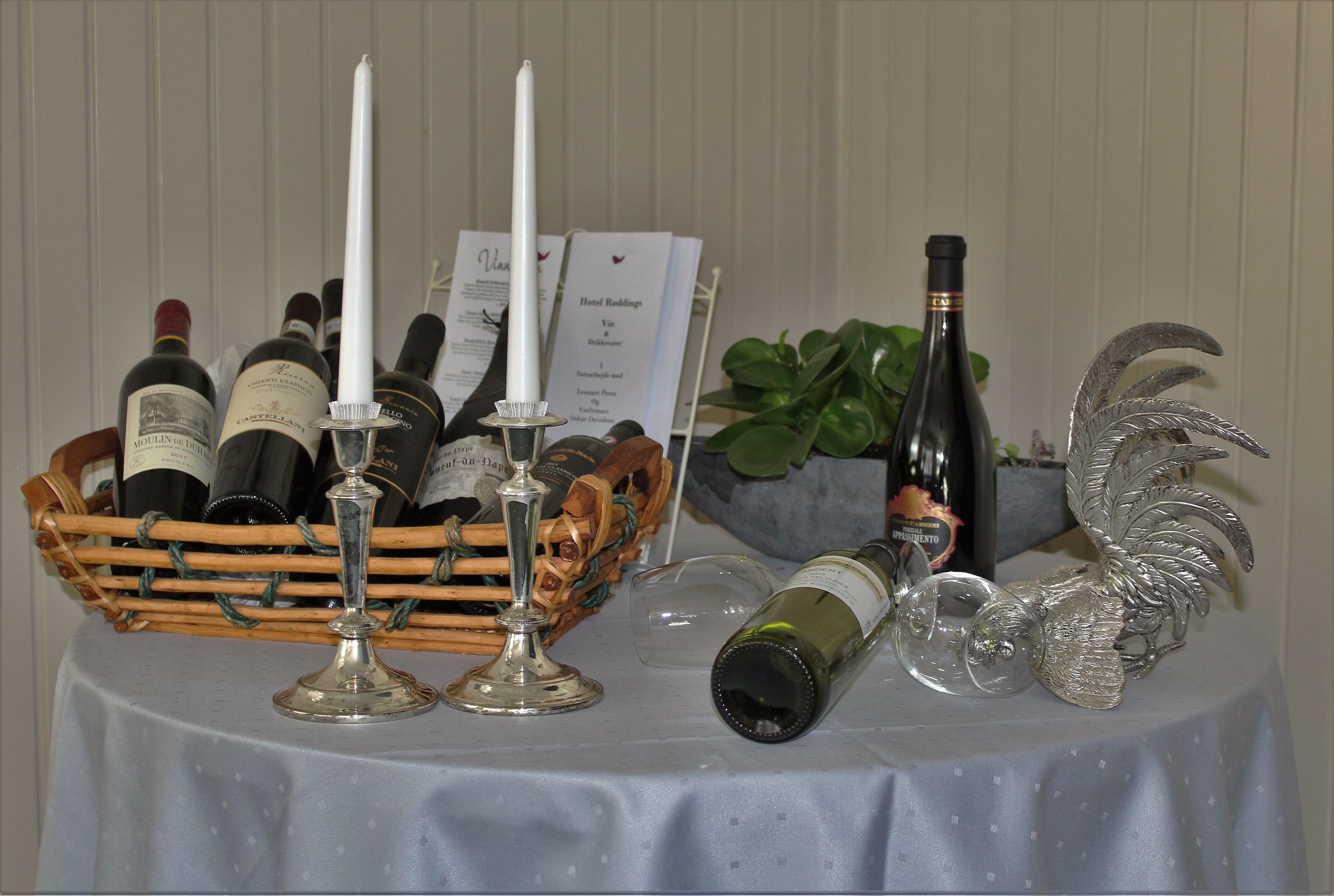 Une table ornée de différentes bouteilles de vin, d’une bougie et d’un panneau indiquant le menu.