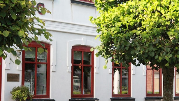 Un edificio blanco con marcos rojos en las ventanas y un árbol en primer plano.