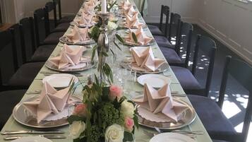 Ein langer Esstisch mit gefalteten Servietten, Tellern und Besteck, begleitet von Stühlen und einer Blumenvase.