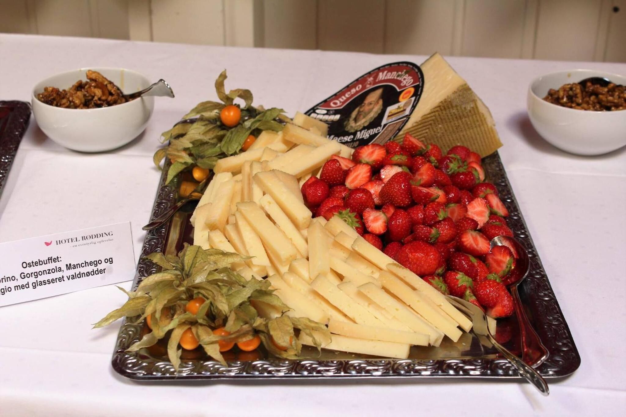 A buffet table with a variety of food items including sliced cheese, strawberries, and a cheese selection sign.