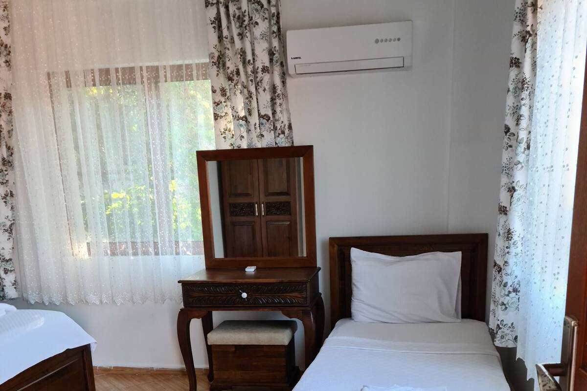 A hotel room with a wooden bed, a wooden nightstand, a wooden dresser, a mirror, and a window with floral curtains.