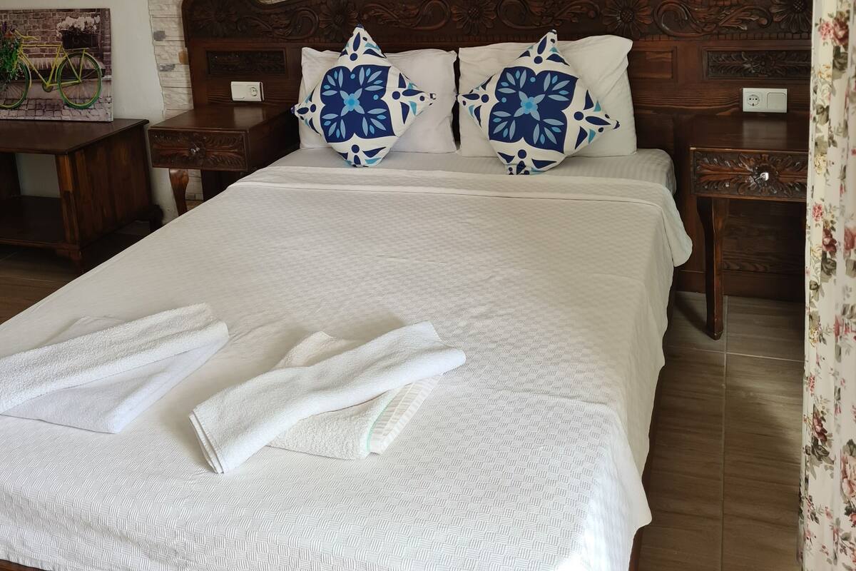 A neatly made bed with white linens and blue patterned pillows, a wooden headboard, and a stone-patterned wall.