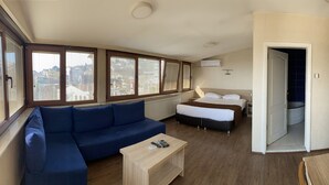 A hotel room with a large bed, a sofa, a TV, and a view of the city through large windows. - Hotel Cenedag (Izmit)