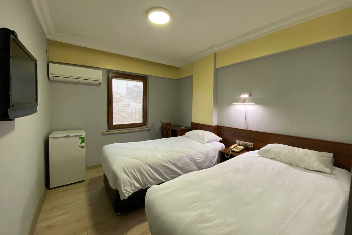 Habitación de hotel con dos camas, un escritorio, una silla, un refrigerador pequeño y una lámpara de noche.