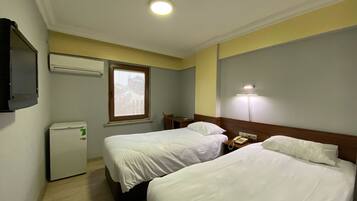 Habitación de hotel con dos camas, un escritorio, una silla, un refrigerador pequeño y una lámpara de noche.