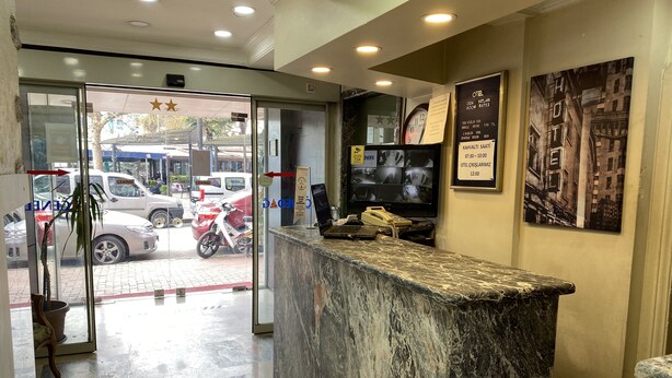 A hotel reception area with a marble counter, a security camera, and a wall-mounted TV displaying room rates. - Hotel Cenedag (Izmit)