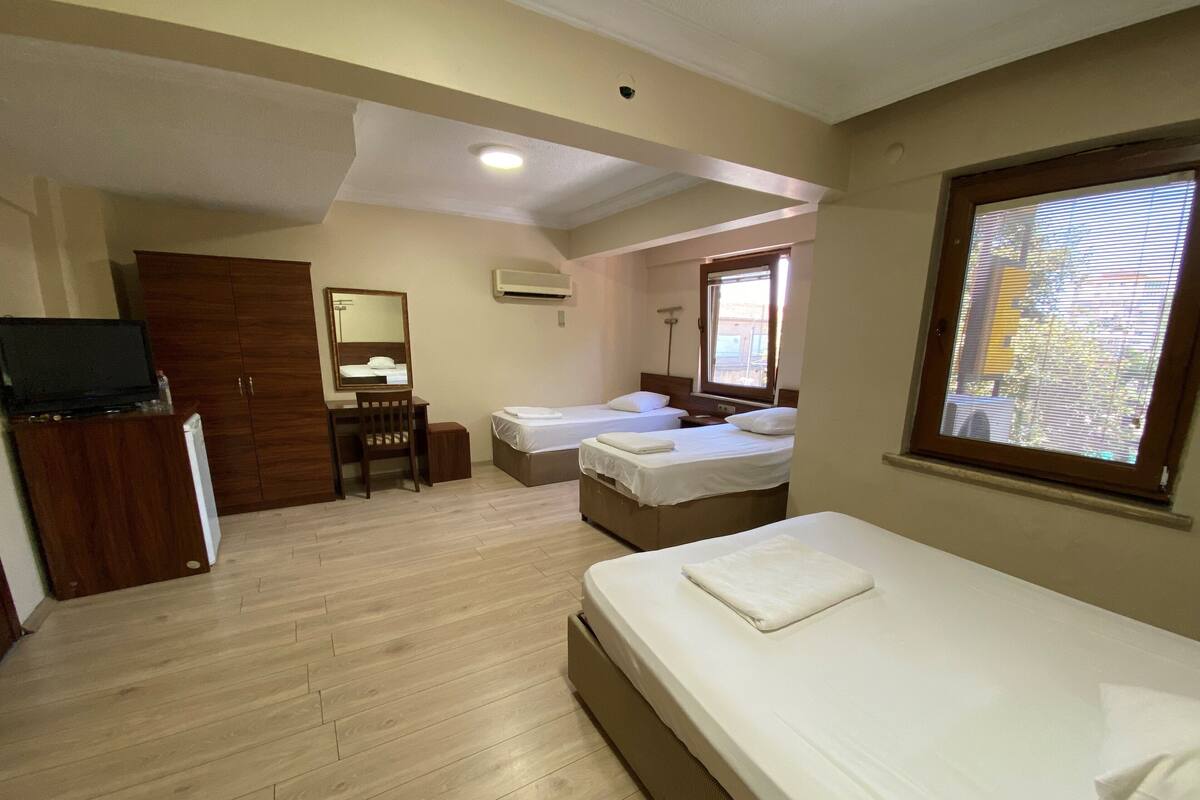 Habitación de hotel con dos camas, un escritorio con silla, armario, televisor y ventana con persianas.