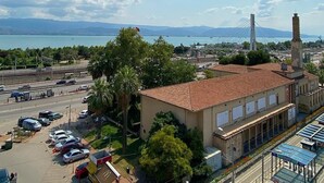 A building with a red-tiled roof, a large chimney, and a view of a bridge and water body in the background. - Hotel Cenedag (Izmit)