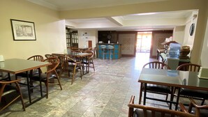 A spacious dining area with multiple wooden tables and chairs, a bar area with stools, and a tiled floor. - Hotel Cenedag (Izmit)