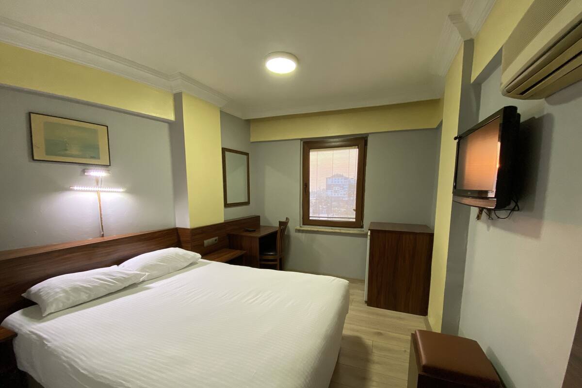 Habitación de hotel con cama, escritorio, silla, televisión y ventana.